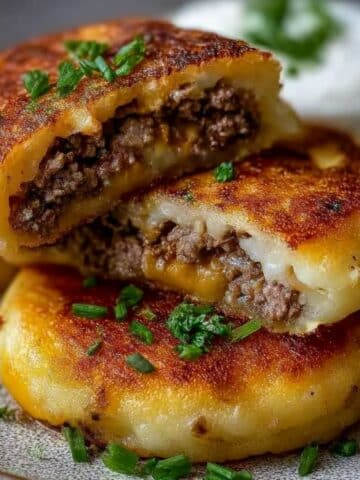 Golden stuffed potato pancakes with ground beef and melted cheese, garnished with fresh chives.