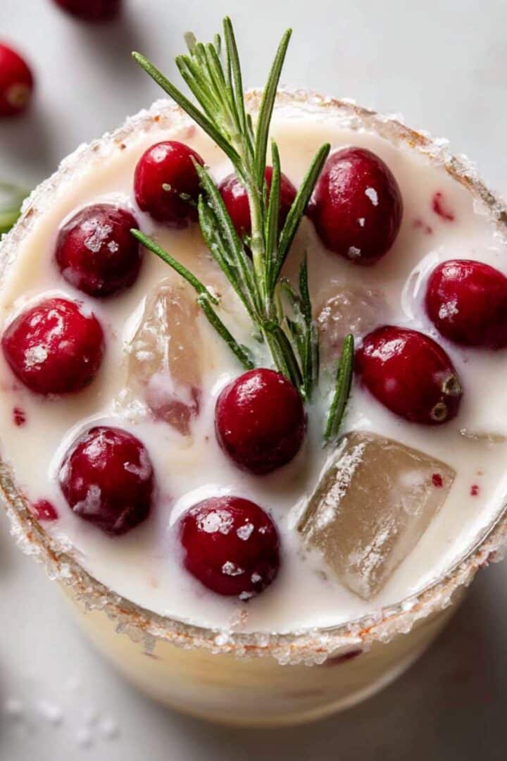 Creamy white Christmas cranberry margarita topped with fresh cranberries and a rosemary sprig in a sugar-rimmed glass