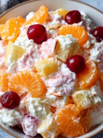 Ambrosia fruit salad with mandarin oranges, pineapple chunks, cherries, coconut, and marshmallows in a creamy dressing.