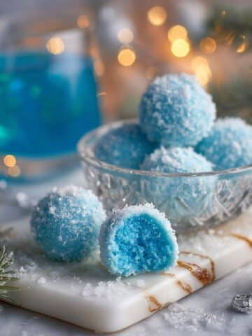 Blue Christmas truffles coated in sparkling blue sugar with a creamy blue center on a white marble board.