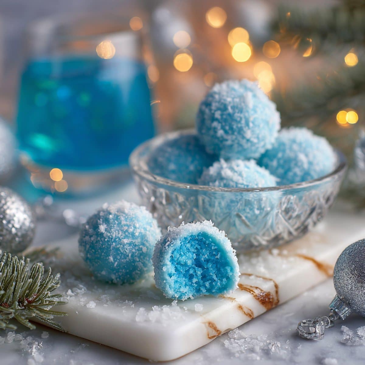 Blue Christmas truffles coated in sparkling blue sugar with a creamy blue center on a white marble board.