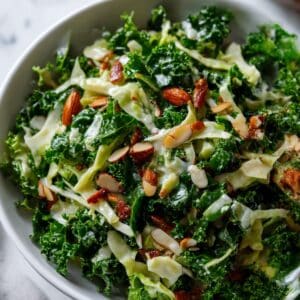 Vibrant Chick fil A kale salad in a white bowl, featuring fresh curly kale, shredded cabbage, and chopped roasted almonds on a white marble surface.