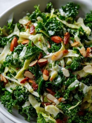 Vibrant Chick fil A kale salad in a white bowl, featuring fresh curly kale, shredded cabbage, and chopped roasted almonds on a white marble surface.