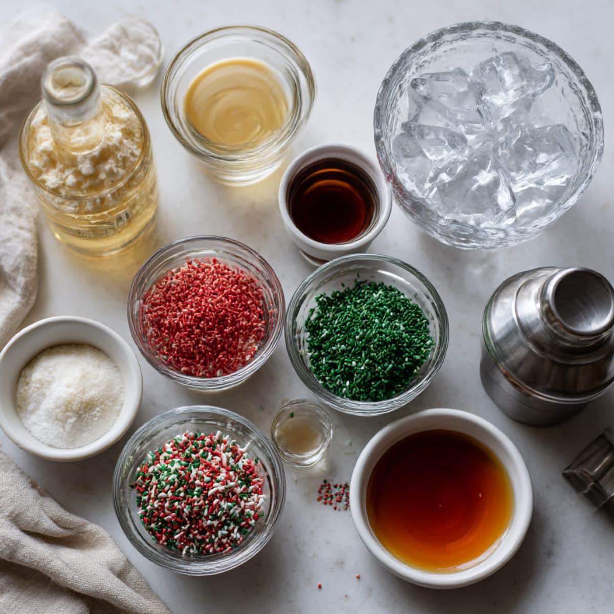 Ingredients for Christmas sugar cookie shots arranged on a white kitchen counter, including vodka, amaretto, Irish cream, and festive sprinkles.