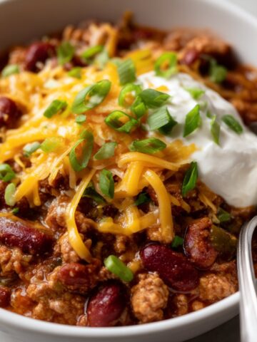 Hearty homemade chili with ground beef, kidney beans, melted cheddar cheese, sour cream, and green onions in a bowl.