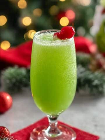 Grinch mimosa cocktail in a champagne flute with bright green color and cherry garnish on a festive Christmas table.
