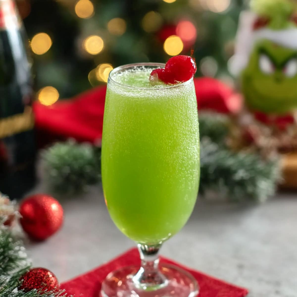 Grinch mimosa cocktail in a champagne flute with bright green color and cherry garnish on a festive Christmas table.