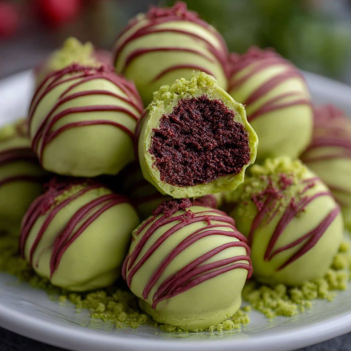 Grinch Oreo truffles coated in green chocolate with red drizzle, one truffle cut open showing red velvet Oreo filling.