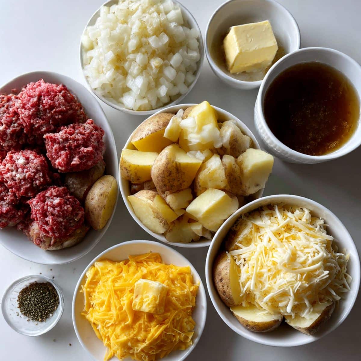 Overhead view of ingredients for hamburger and potato casserole including beef, potatoes, cheese, onions, and spices.