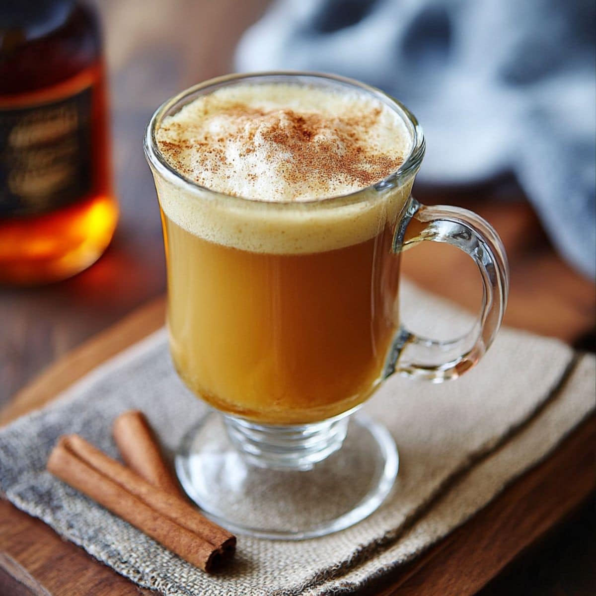 Warm homemade hot buttered rum in a glass mug topped with cinnamon foam. Cozy winter rum cocktail made with spiced butter batter and dark rum.