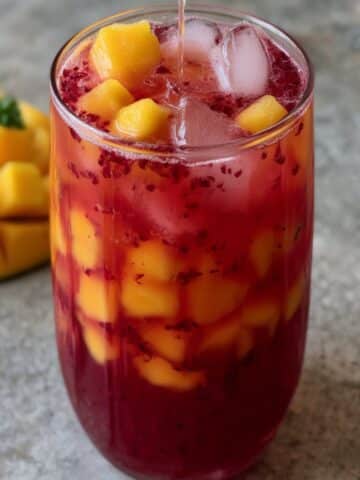 Homemade mango hibiscus iced tea with vibrant ruby hibiscus and fresh mango chunks over ice.