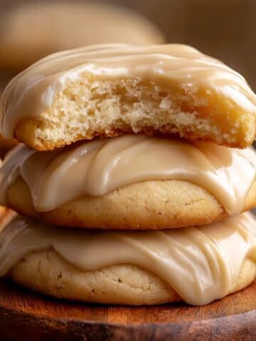 Stack of soft maple cookies topped with glossy brown butter icing, with the top cookie bitten to reveal a tender, moist interior.