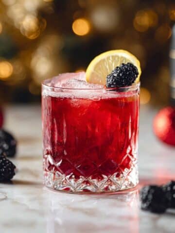 Merry berry bourbon cocktail served over ice with blackberry and lemon garnish