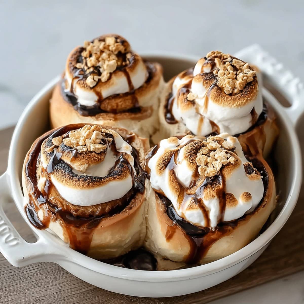 S’mores Rolls in a white baking dish with toasted marshmallows, melted chocolate drizzle, and graham cracker crumbs.
