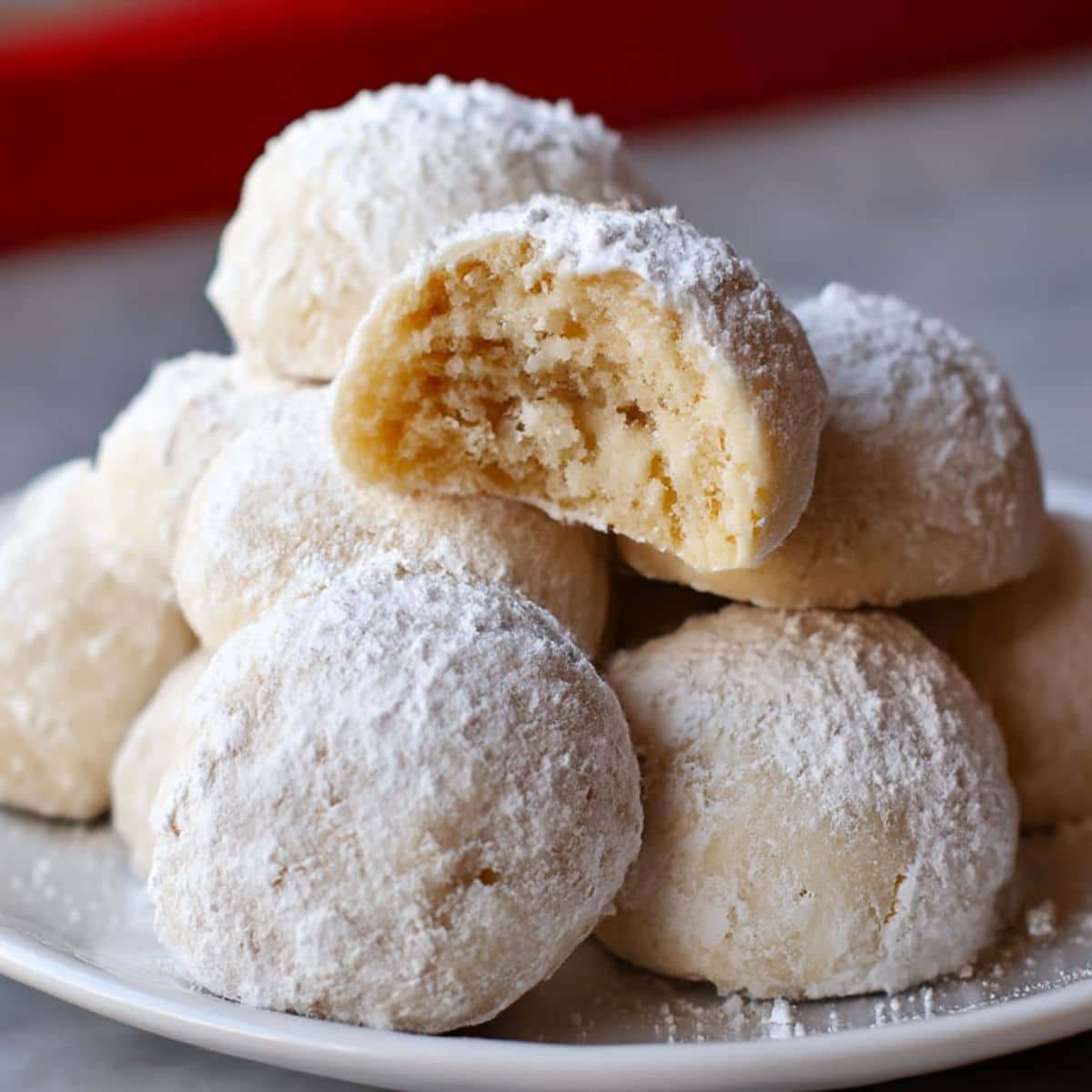 Homemade snowball cookies coated in powdered sugar on a white plate.