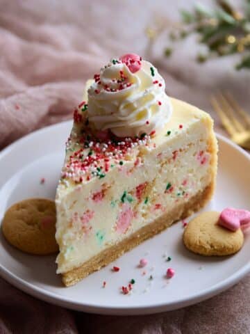 Slice of sugar cookie cheesecake with creamy vanilla filling, festive sprinkles, and a buttery sugar cookie crust on a white plate.