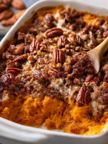 Sweet potato casserole with buttery pecan streusel topping baked until golden and bubbly in a white baking dish.