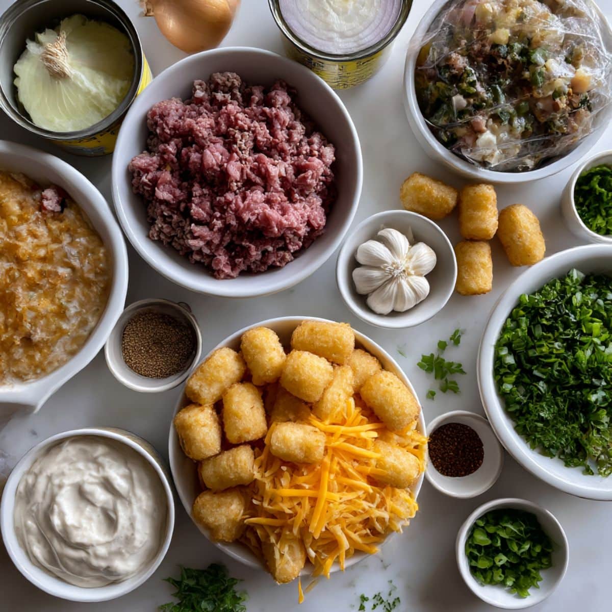 Overhead view of ingredients for tater tot casserole including ground beef, veggies, soup, cheese, and frozen tater tots.