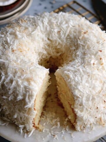 Tom Cruise Coconut Cake with thick white frosting and shredded coconut, sliced to show the moist vanilla cake crumb.