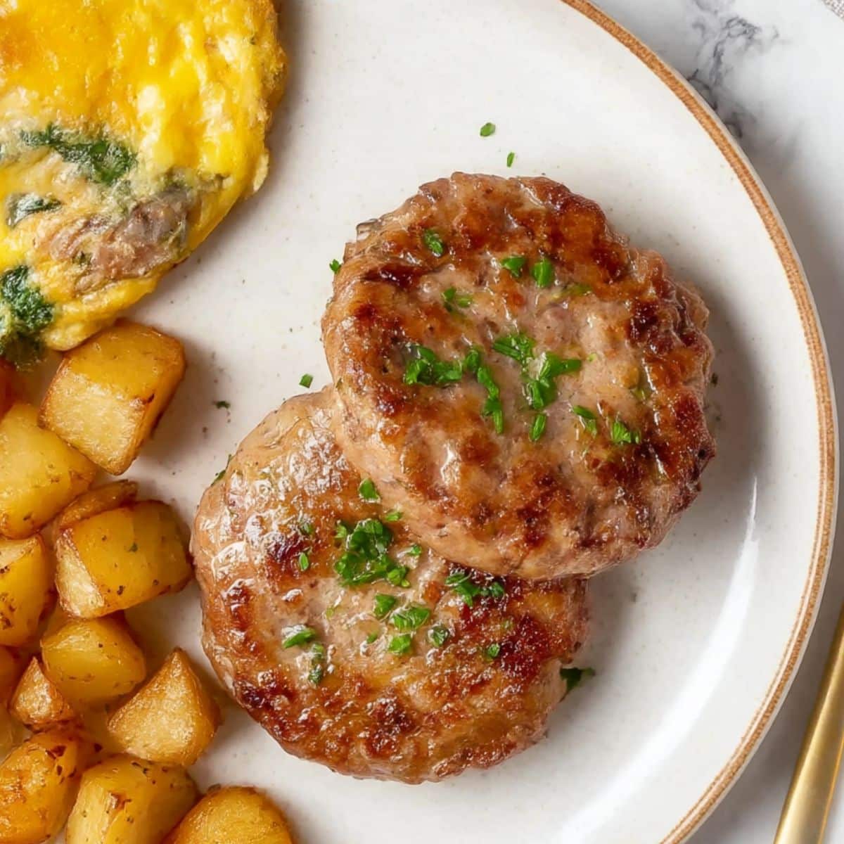 Turkey Breakfast Sausage patties on a white plate with crispy breakfast potatoes and omelet, sprinkled with chopped herbs.