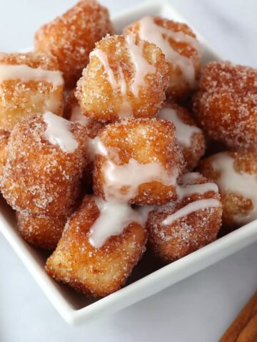Angel cake churro bites coated in cinnamon sugar and drizzled with sweet vanilla glaze, served in a white bowl.