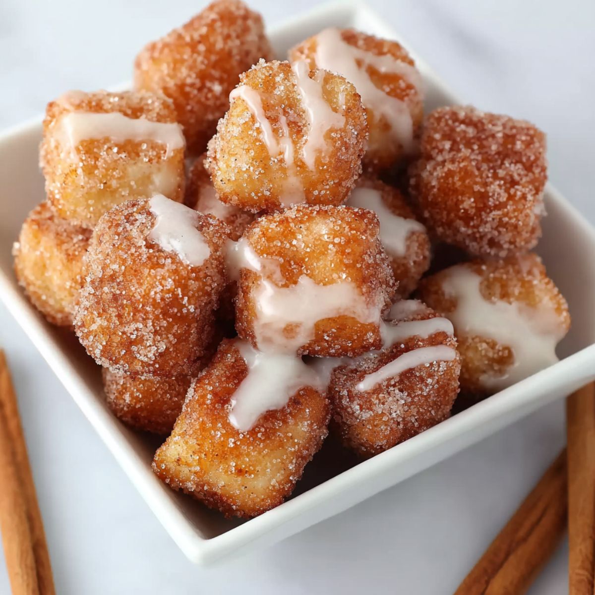 Angel cake churro bites coated in cinnamon sugar and drizzled with sweet vanilla glaze, served in a white bowl.