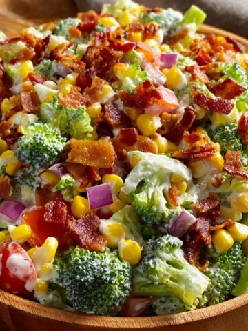 Bacon ranch chopped salad in a wooden bowl with crispy bacon bits, fresh broccoli florets, chopped iceberg lettuce, sweet corn, diced red onions, cherry tomatoes, and creamy ranch dressing