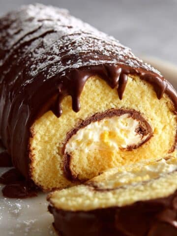 Boston cream roll cake with fluffy vanilla sponge rolled around creamy custard filling and topped with rich chocolate ganache, dusted lightly with powdered sugar.