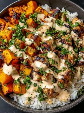 Chicken and sweet potato bowl with roasted chicken pieces, caramelized sweet potatoes, fluffy rice, fresh herbs, and creamy sauce drizzled on top