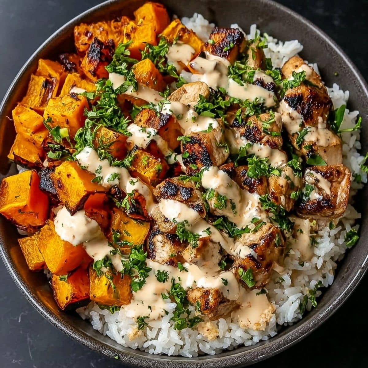 Chicken and sweet potato bowl with roasted chicken pieces, caramelized sweet potatoes, fluffy rice, fresh herbs, and creamy sauce drizzled on top