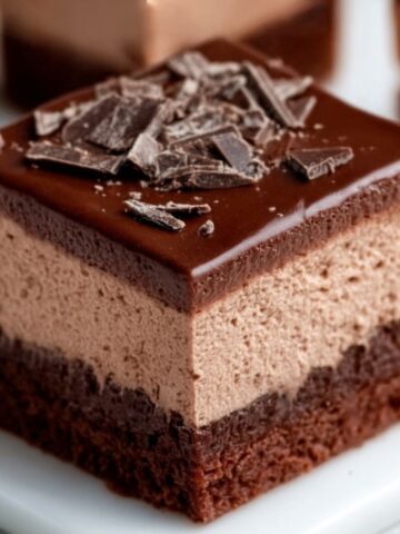 Chocolate mousse brownies with three rich layers—fudgy brownie base, creamy chocolate mousse center, and glossy chocolate ganache topped with chocolate shavings.