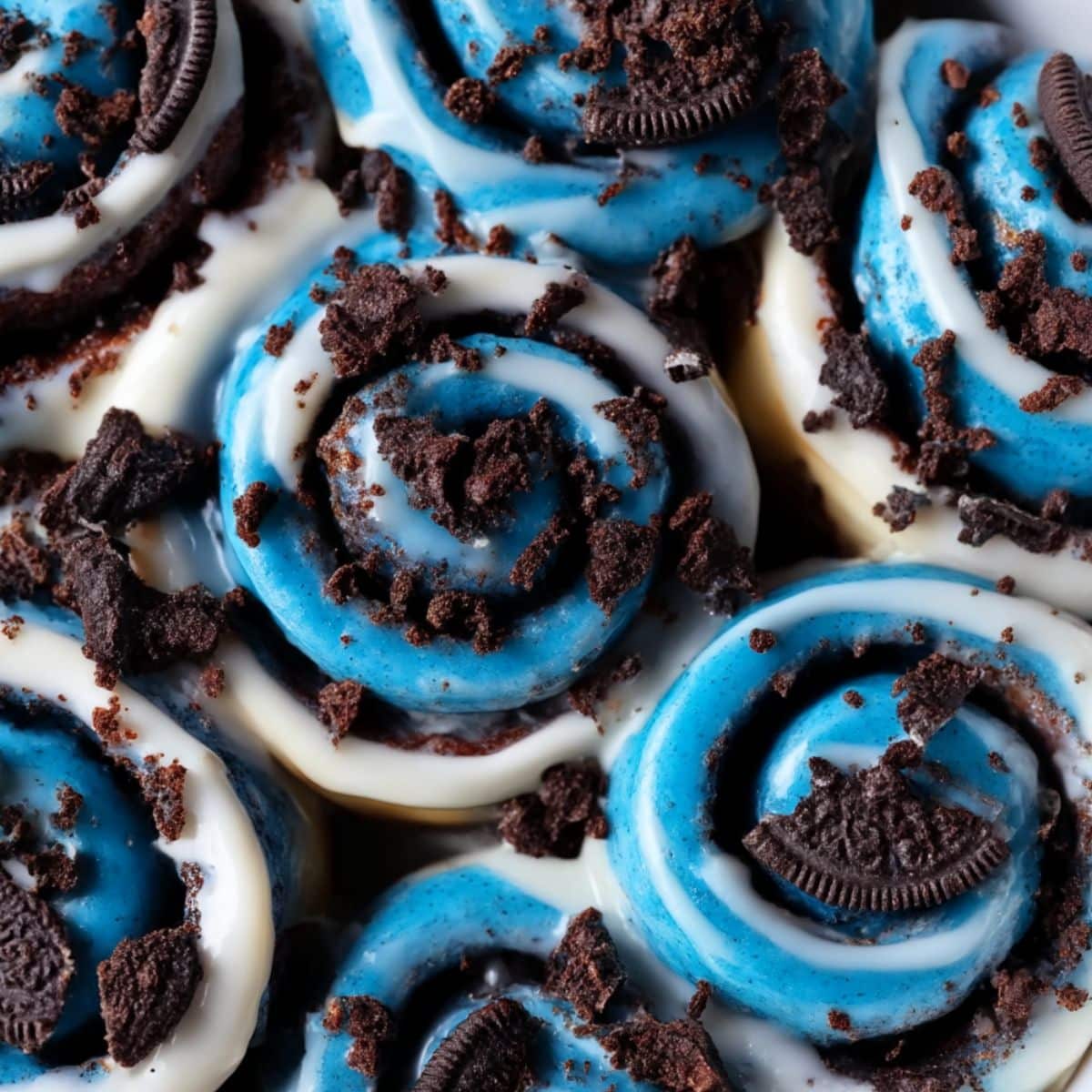 Overhead view of Cookie Monster cinnamon rolls with vivid blue icing, creamy white glaze, and Oreo cookie crumbs sprinkled on top.