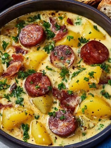 Creamy kielbasa potato soup featuring sliced smoked sausage, tender potato chunks, crispy bacon pieces, and fresh parsley in a rich, velvety broth, served warm with crusty bread on the side.