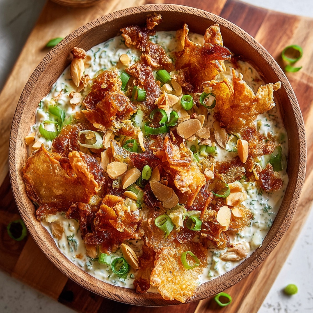 Crispy smashed potato salad served in a rustic wooden bowl with ultra-crispy roasted smashed potatoes over creamy herb-flecked dressing, garnished with crispy bacon bits, toasted sliced almonds, and fresh sliced green onions on a wooden board