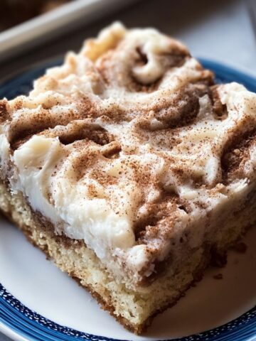 Easy cinnamon roll poke cake with fluffy vanilla cake soaked in cinnamon sugar and topped with thick cream cheese frosting, finished with a dusting of ground cinnamon.