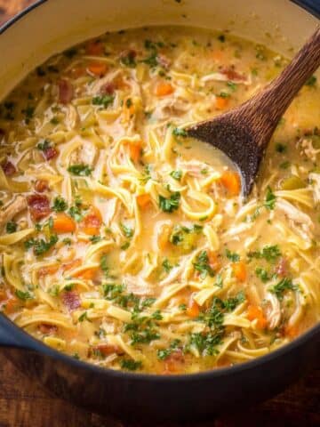 Easy crack chicken noodle soup simmering in a Dutch oven with tender shredded chicken, bacon, egg noodles, carrots, celery, and fresh herbs in a creamy golden broth.