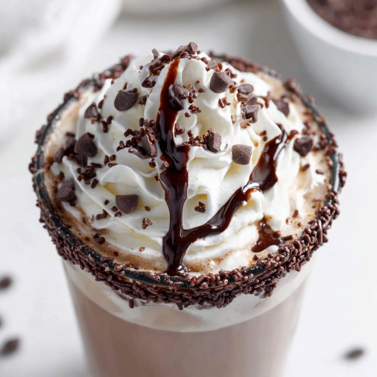 Easy Dirty Snowman hot chocolate topped with whipped cream, chocolate drizzle, mini chocolate chips, and a chocolate sprinkle–rimmed glass.