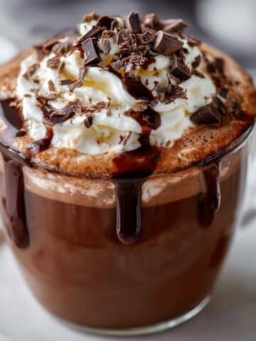 Easy French hot chocolate in a clear glass mug, topped with whipped cream, chocolate shavings, and rich melted chocolate dripping down the sides.
