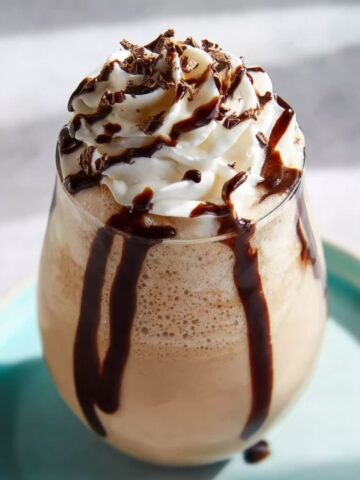 Chocolate milkshake with whipped cream and chocolate syrup drizzles, served in a glass on a turquoise plate.