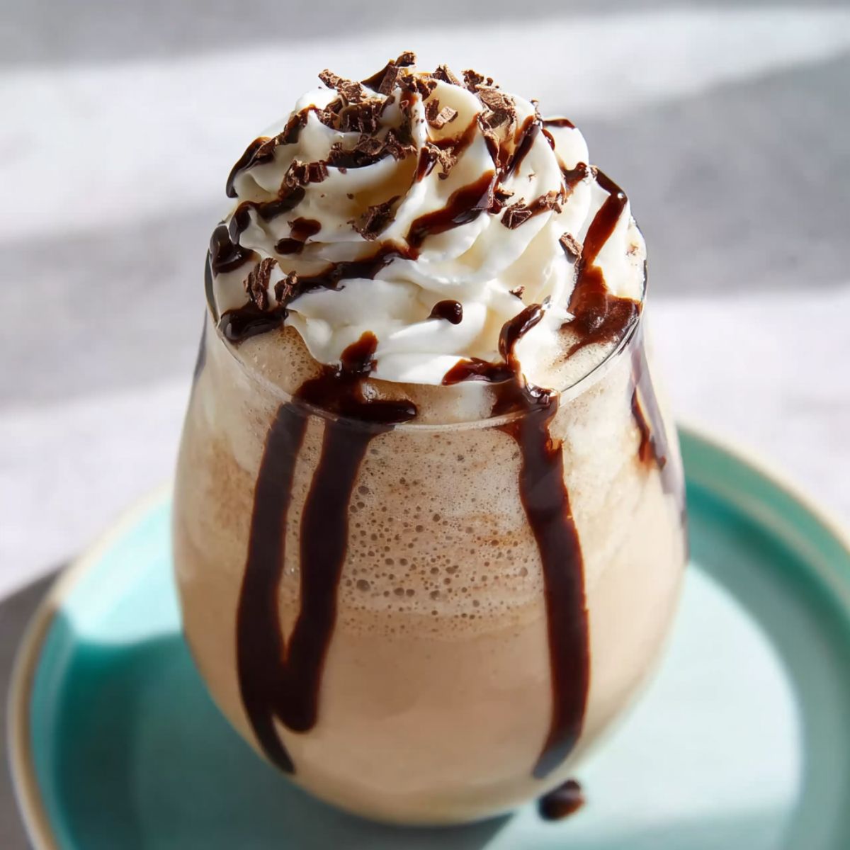 Chocolate milkshake with whipped cream and chocolate syrup drizzles, served in a glass on a turquoise plate.