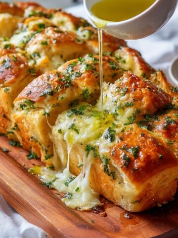 Easy Hawaiian roll garlic bread with melted mozzarella and herbs, featuring a gooey cheese pull as warm garlic butter is poured over the rolls