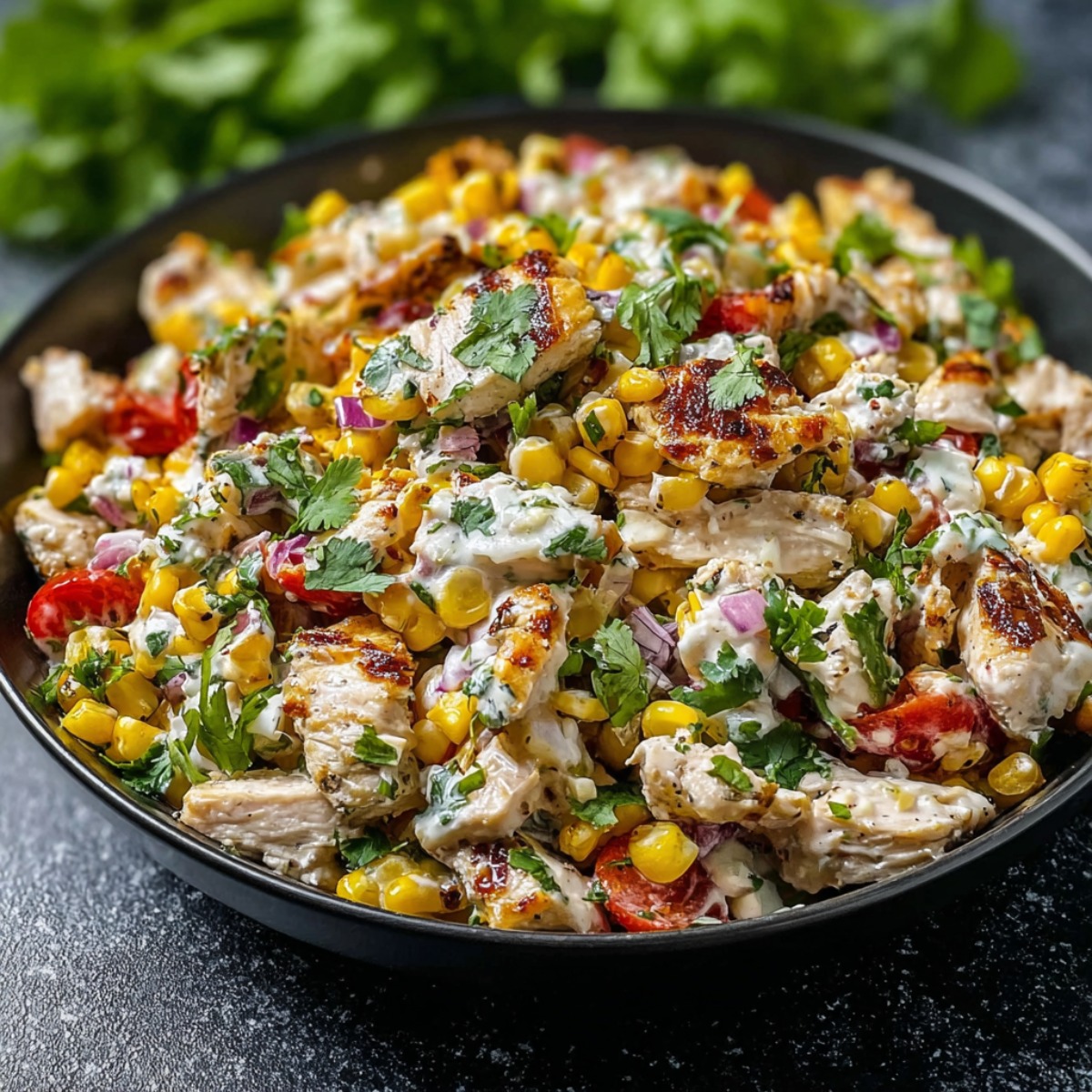 Mexican street corn chicken salad in a black bowl featuring grilled chicken pieces, charred sweet corn kernels, diced red bell peppers, red onions, fresh cilantro, and creamy cilantro-lime dressing