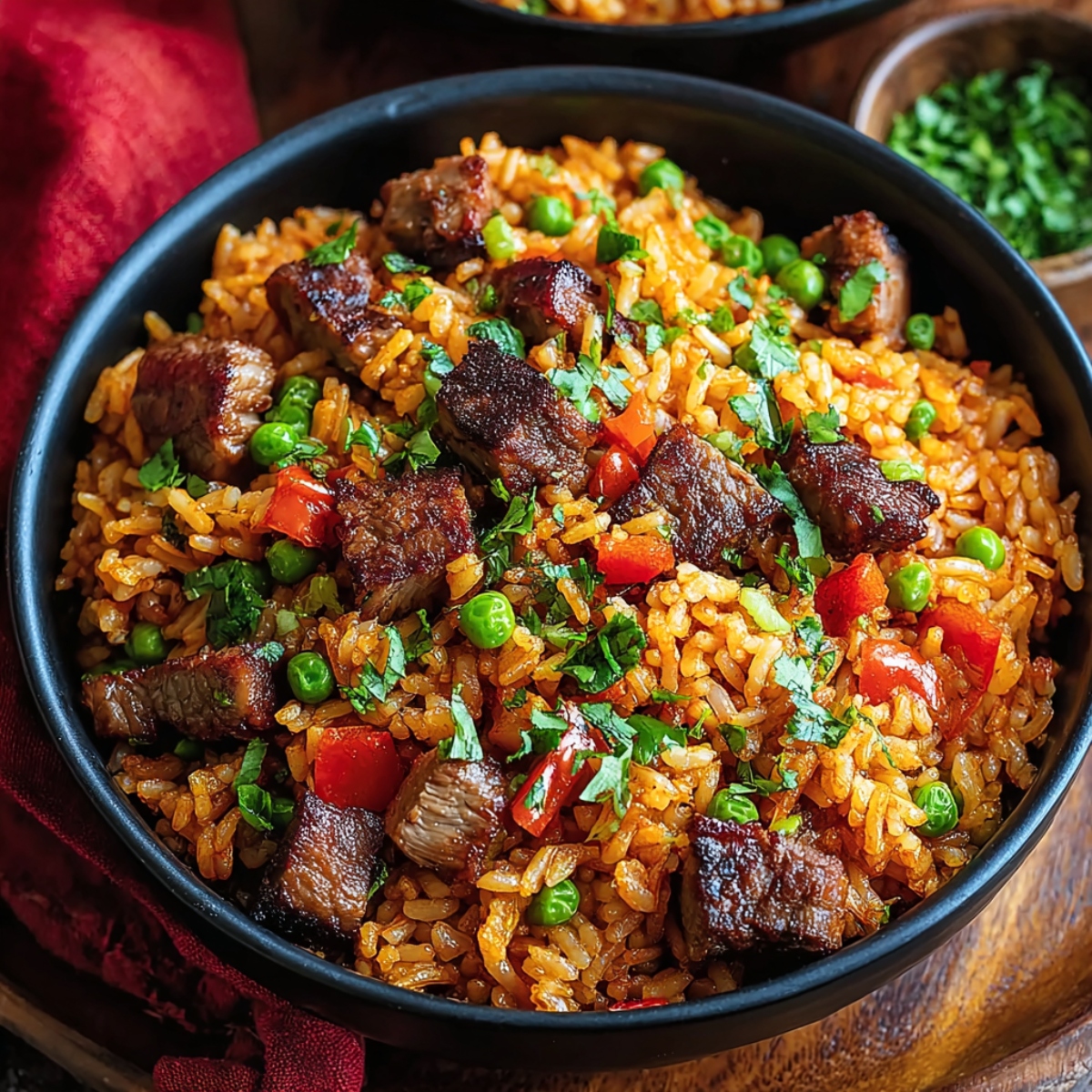 Seasoned rice with caramelized steak chunks, green peas, diced red bell peppers, and fresh cilantro in a black skillet on a wooden board with a red plaid napkin.