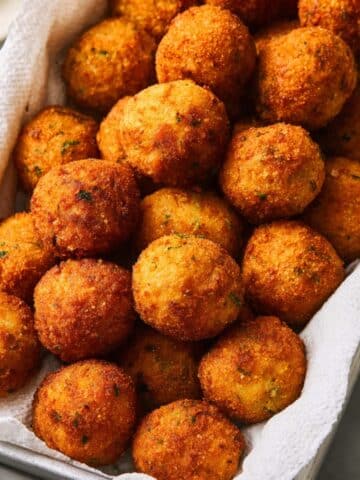 Crispy fried rice balls with a golden, crunchy coating, piled in a paper-lined basket and freshly cooked until perfectly browned and crunchy.