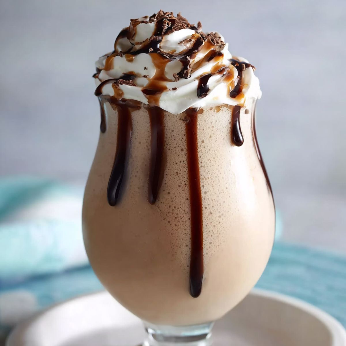 Creamy chocolate milkshake in a glass, topped with whipped cream, chocolate drizzle, and chocolate shavings.