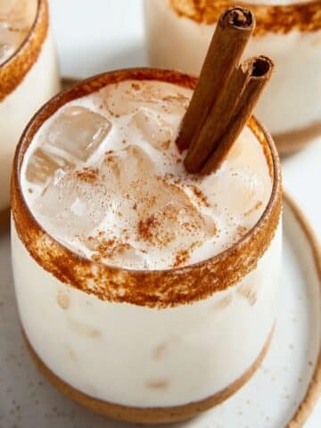 Creamy horchata drink over ice with cinnamon sticks and cinnamon sugar rim