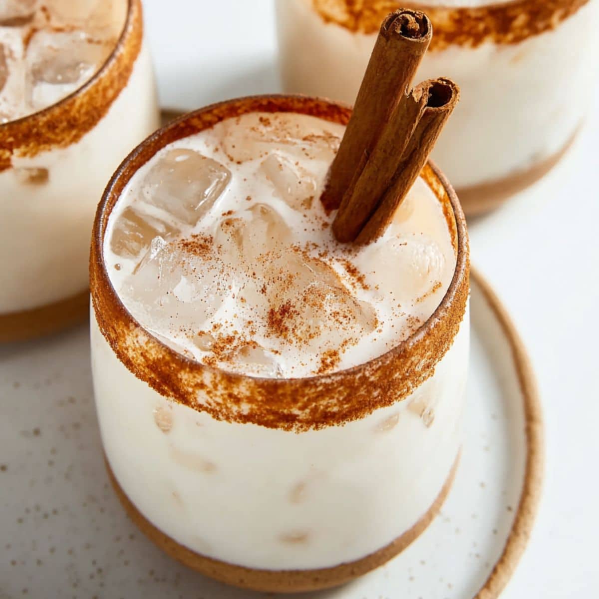 Creamy horchata drink over ice with cinnamon sticks and cinnamon sugar rim