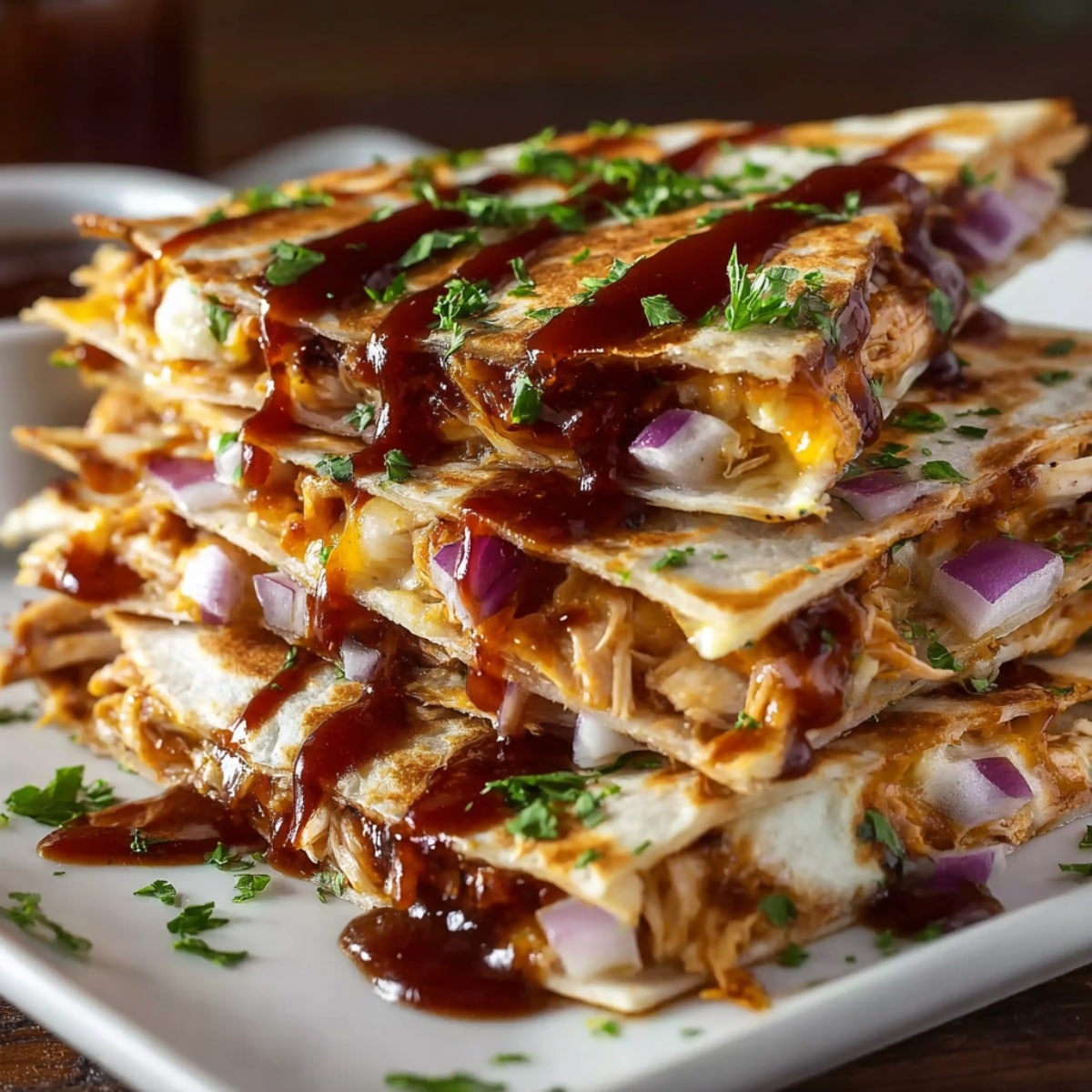 Hot honey BBQ chicken quesadillas stacked on a plate with shredded chicken, melted cheese, red onions, fresh herbs, and rich barbecue sauce drizzled on top