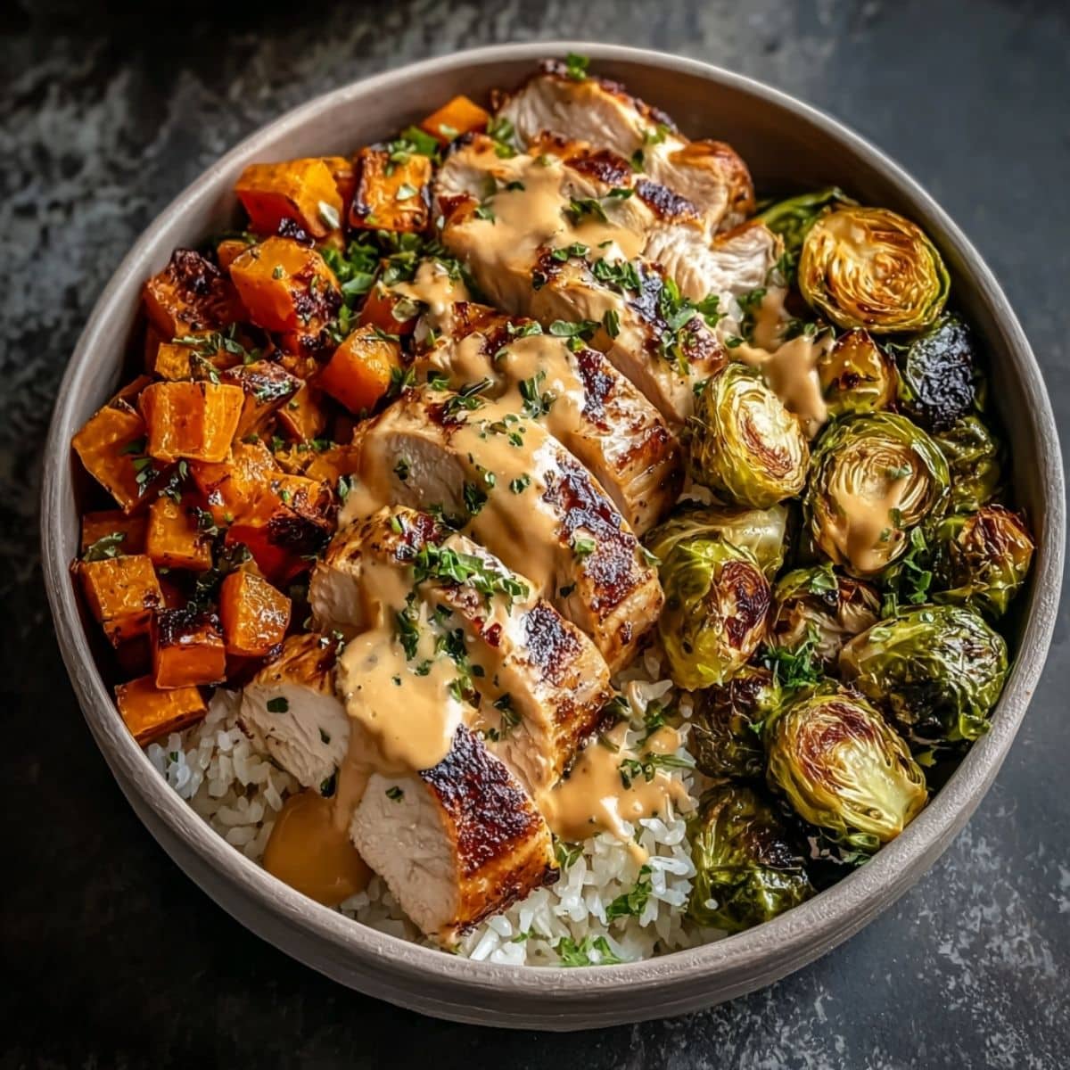 Maple Dijon chicken bowl with sliced roasted chicken, sweet potatoes, Brussels sprouts, and rice drizzled with creamy maple Dijon sauce