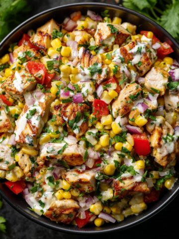 Mexican street corn chicken salad in a black bowl with grilled chicken pieces, sweet corn kernels, diced red bell peppers, red onions, fresh cilantro, and creamy cilantro-lime dressing
